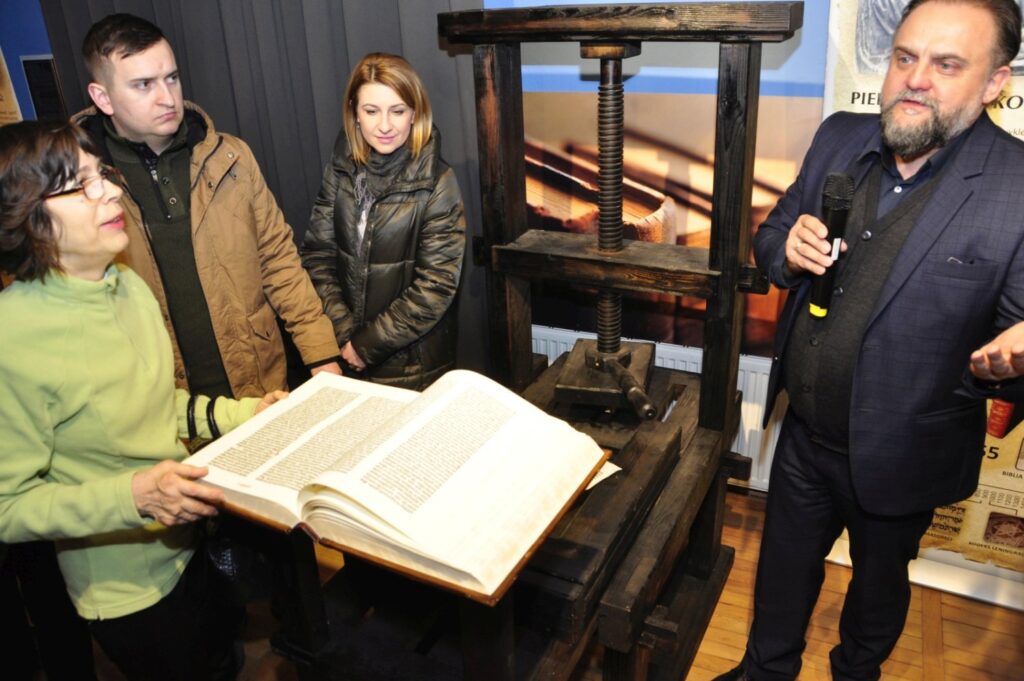 Kurator prezentuje rekonstrukcję dawnej prasy drukarskiej oraz otwartą księgę, wyjaśniając proces powstawania pierwszych drukowanych wydań Biblii (kliknięcie powiększy zdjęcie).