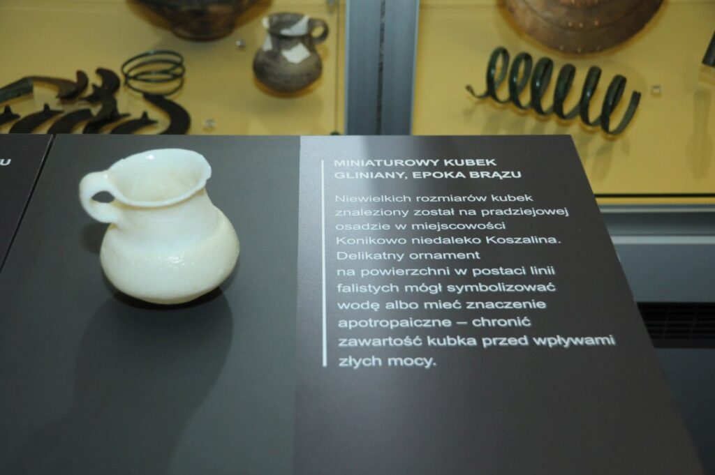 Zbliżenie na kopię glinianego kubka wykonaną w druku 3D wraz z opisem wyjaśniającym jego pochodzenie i przypuszczalne przeznaczenie (kliknięcie powiększy zdjęcie).