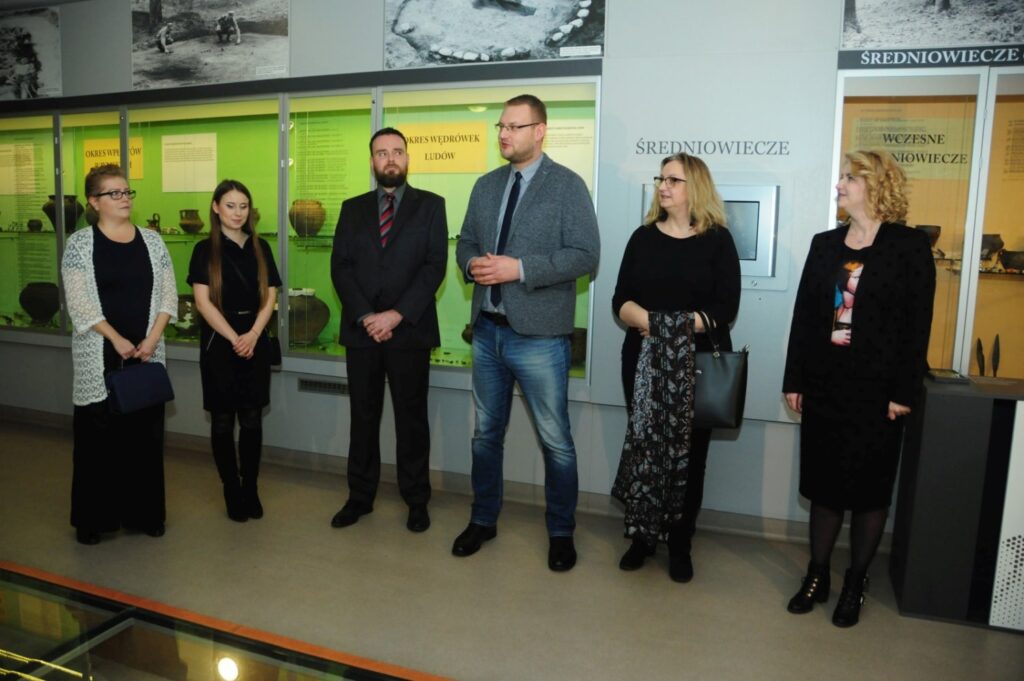 Organizatorzy i kuratorzy witają gości podczas otwarcia wystawy archeologicznej na tle gablot prezentujących zabytki z wykopalisk oraz plansz poświęconych najstarszym dziejom regionu (kliknięcie powiększy zdjęcie).