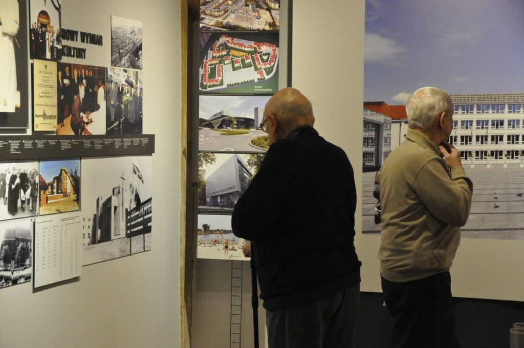 Dwóch zwiedzających uważnie ogląda plansze prezentujące archiwalne fotografie oraz współczesne zdjęcia miejsc związanych z historią Koszalina. Ekspozycja zestawia materiały historyczne z obecnym wyglądem miasta (kliknięcie powiększy zdjęcie).