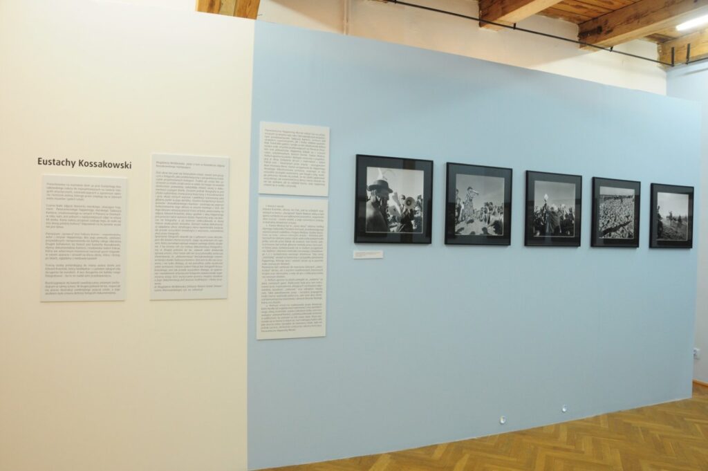 Fragment ekspozycji poświęcony twórczości Eustachego Kossakowskiego. Na jasnoniebieskiej ścianie zaprezentowano tekst biograficzny oraz serię czarno-białych fotografii dokumentujących wydarzenia artystyczne i społeczne, oprawionych w czarne ramy (kliknięcie powiększy zdjęcie).