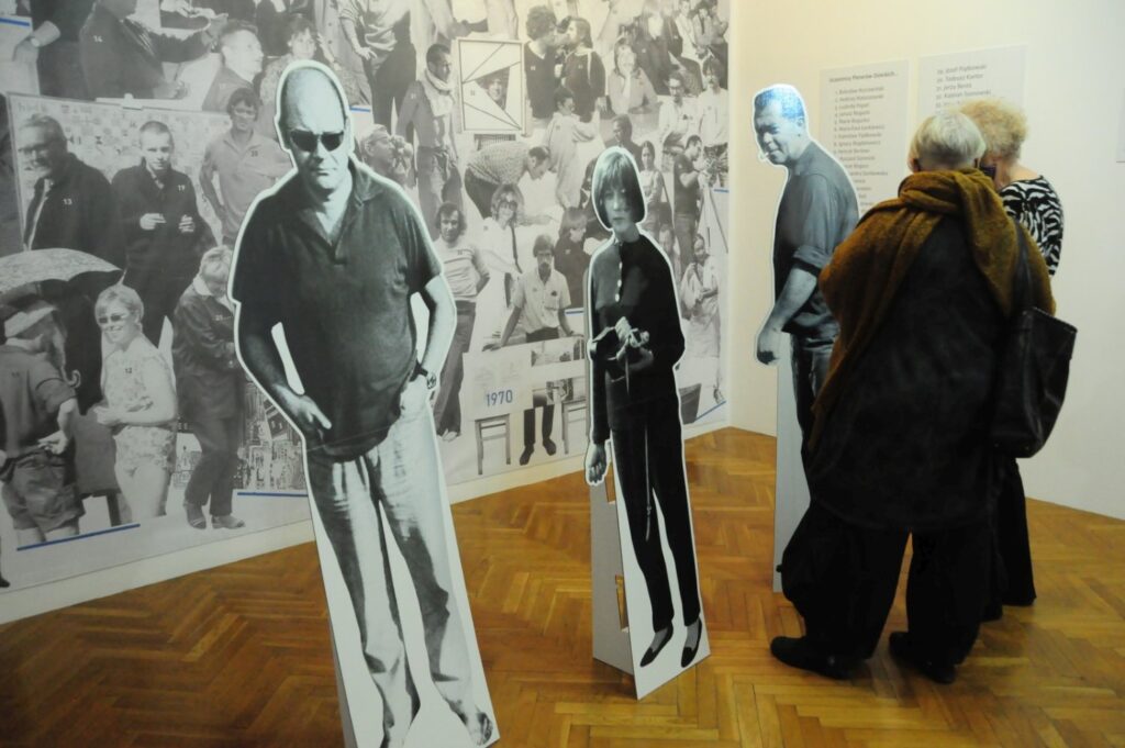 Zwiedzający zatrzymują się przed wielkoformatowym fotomontażem oraz sylwetkami postaci wykonanymi w naturalnej wielkości; instalacja nawiązuje do historii i pamięci, stanowiąc jedną z części prezentowanej wystawy sztuki współczesnej (kliknięcie powiększy zdjęcie).