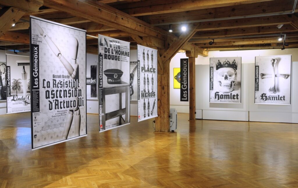 Fragment wystawy z szeregiem wielkoformatowych czarno-białych plakatów przedstawiających motywy i tytuły związane z filmem oraz teatrem; ekspozycja znajduje się w przestrzeni z drewnianą konstrukcją stropu (kliknięcie powiększy zdjęcie).