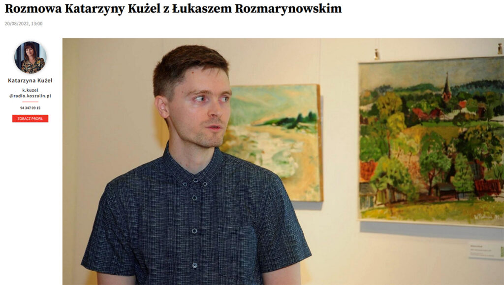 Mężczyzna stojący w sali wystawowej na tle dwóch kolorowych obrazów pejzażowych patrzy w bok obok widoczny panel artykułu z danymi Katarzyny Kużel.