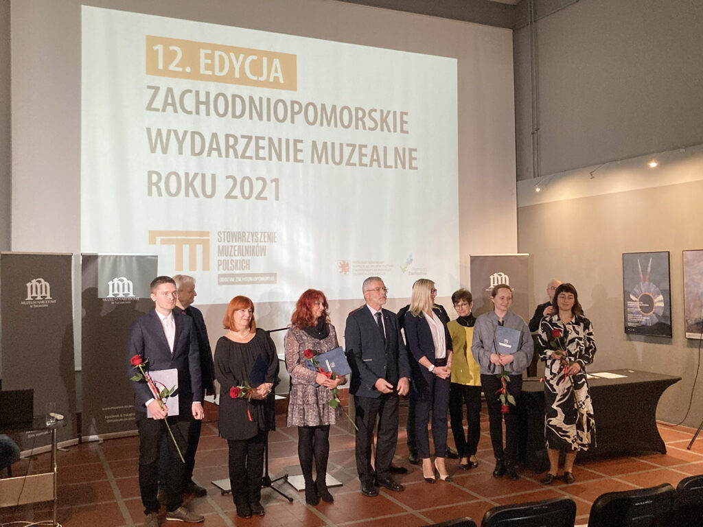 Laureaci dwunastej edycji konkursu na Zachodniopomorskie Wydarzenie Muzealne Roku 2021 stoją na scenie i pozują do wspólnego zdjęcia.