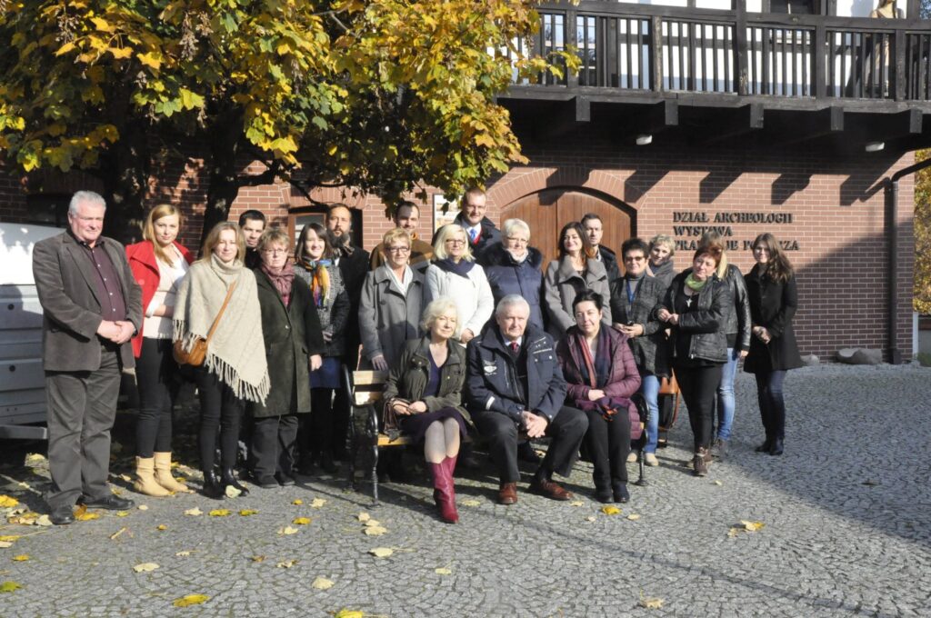 Pracownicy Muzeum w Koszalinie pozująca do wspólnego zdjęcia przed budynkiem muzeum na dziedzińcu w jesiennej scenerii (kliknięcie powiększy zdjęcie).