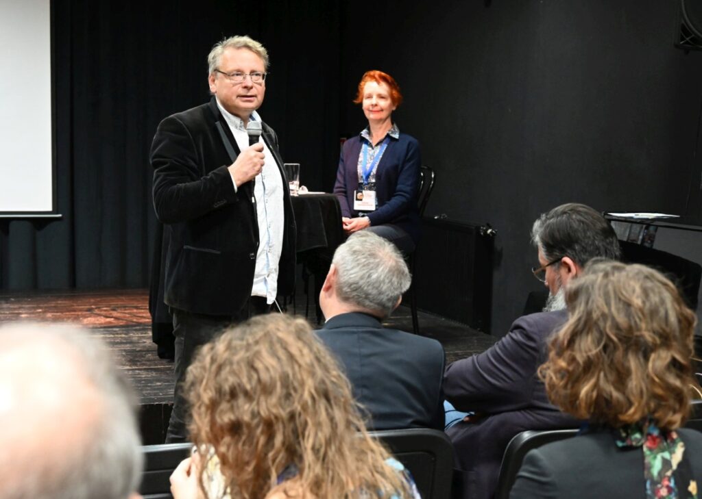 Gość z sali przemawia do uczestników konferencji, a obok stoi organizatorka wydarzenia (kliknięcie powiększy zdjęcie).
