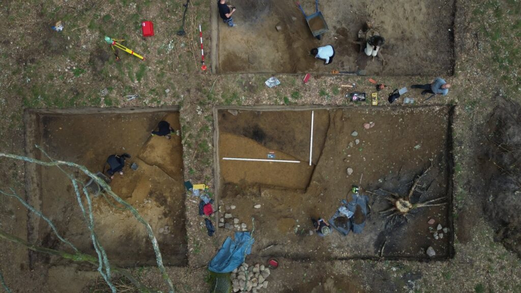 Widok z góry na kilka prostokątnych wykopów archeologicznych z pracującymi badaczami i rozłożonym sprzętem (kliknięcie powiększy zdjęcie).