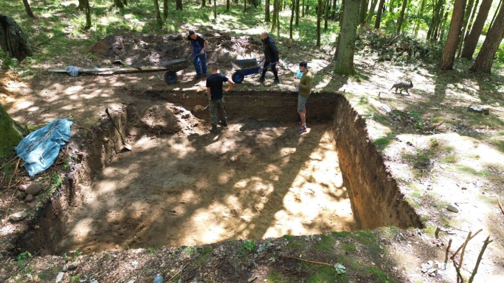 Zespół archeologów pracuje w wykopie wśród drzew, prowadząc badania terenowe (kliknięcie powiększy zdjęcie).