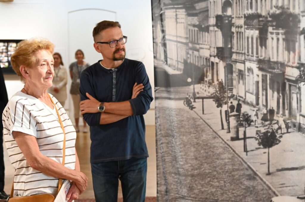 Dwie osoby stoją przed dużą fotografią przedstawiającą ulicę i rozmawiają podczas zwiedzania (kliknięcie powiększy zdjęcie).
