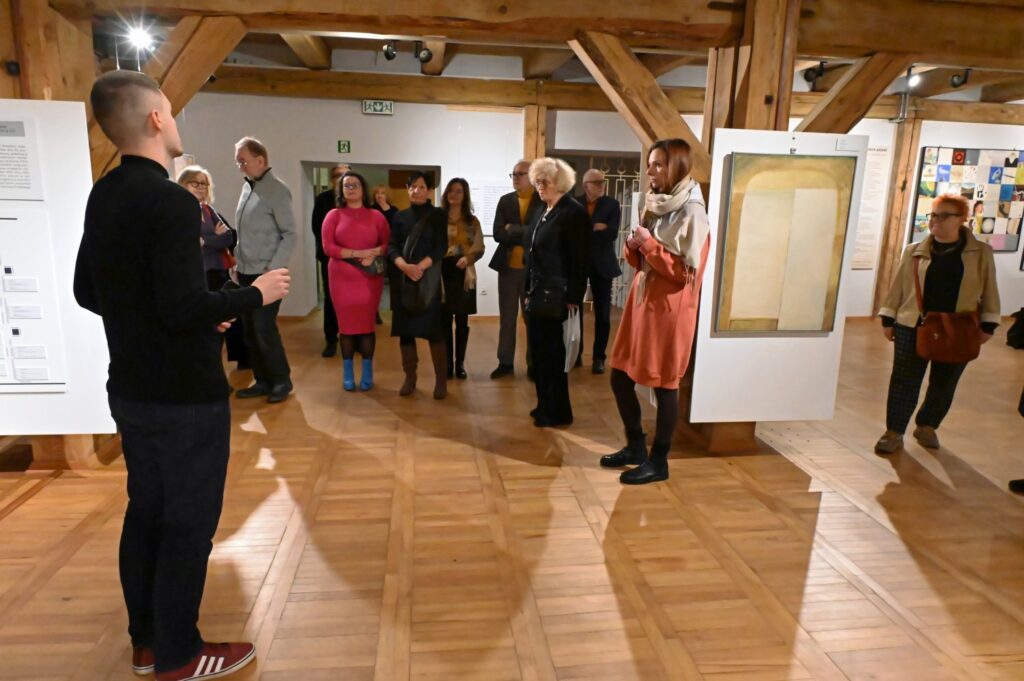 Przewodnik przemawia do grupy zgromadzonej w przestrzeni galerii podczas oprowadzania po wystawie (kliknięcie powiększy zdjęcie).