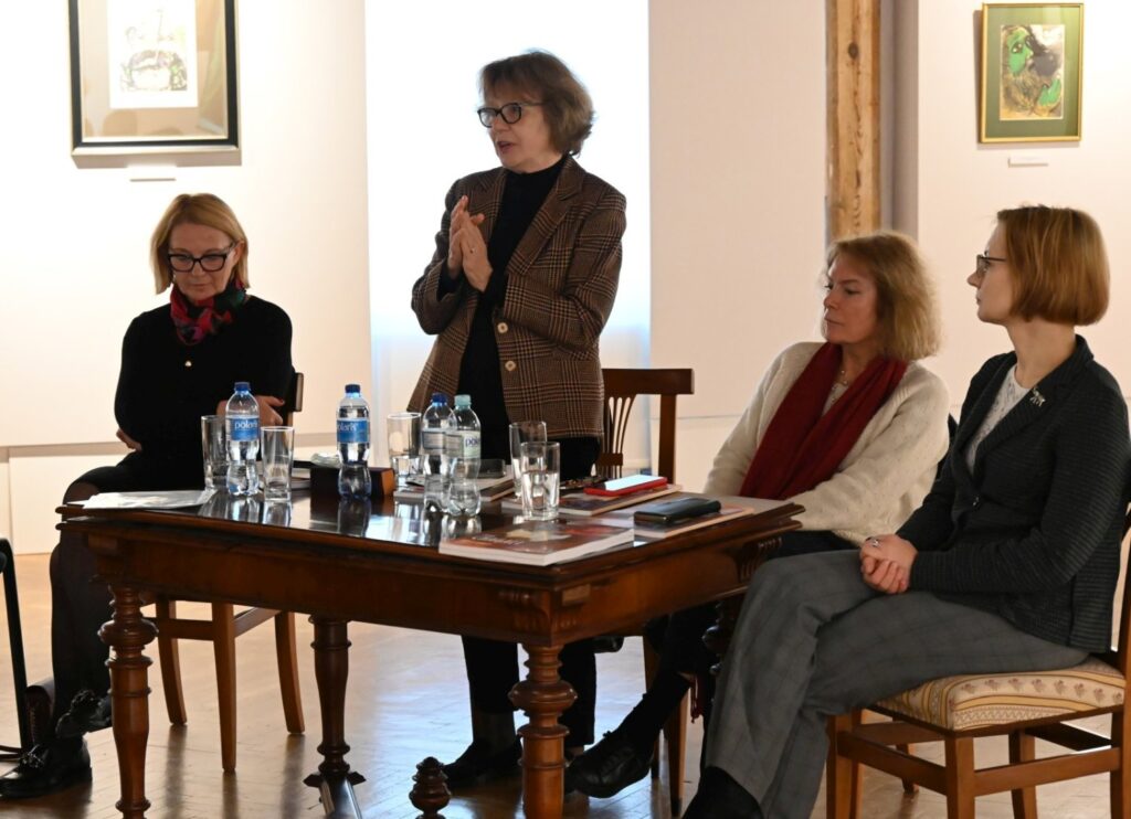 Panel dyskusyjny przy stole z trzema kobietami jedna z nich przemawia a pozostałe słuchają (kliknięcie powiększy zdjęcie).