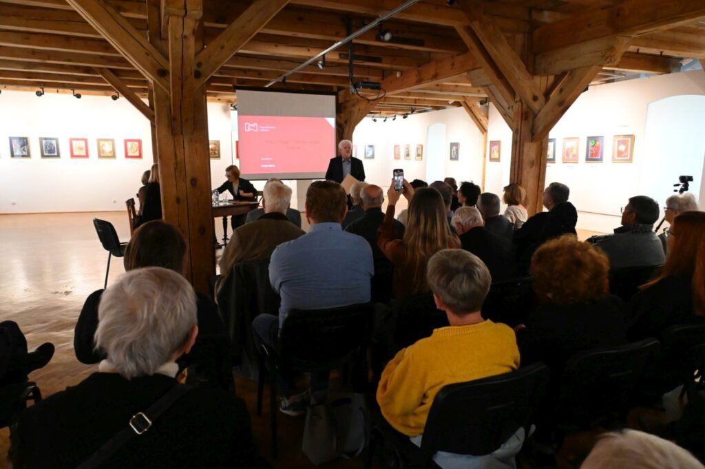 Sala wystawowa wypełniona uczestnikami konferencji oglądającymi prezentację wyświetlaną na ekranie (kliknięcie powiększy zdjęcie).