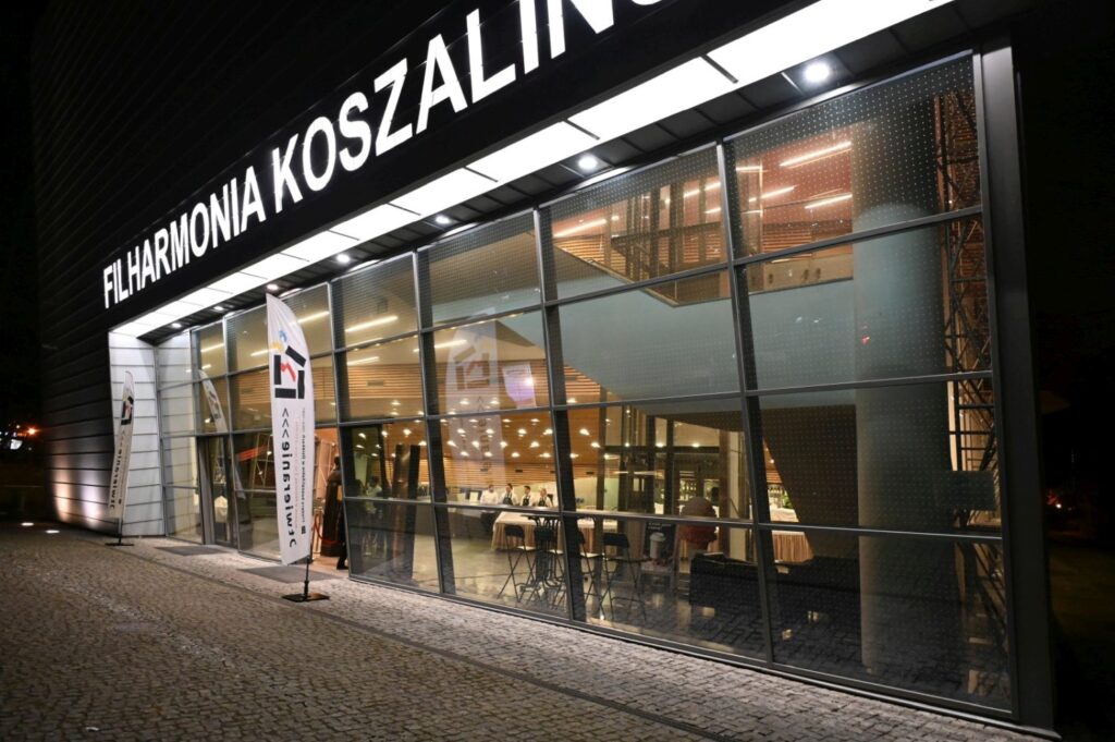 Nocny widok na przeszklony budynek Filharmonii Koszalińskiej z oświetlonym wnętrzem i wejściem (kliknięcie powiększy zdjęcie).