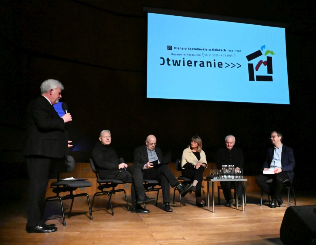 Panel dyskusyjny na scenie z kilkoma osobami siedzącymi na krzesłach obok ekran z napisem Otwieranie (kliknięcie powiększy zdjęcie).