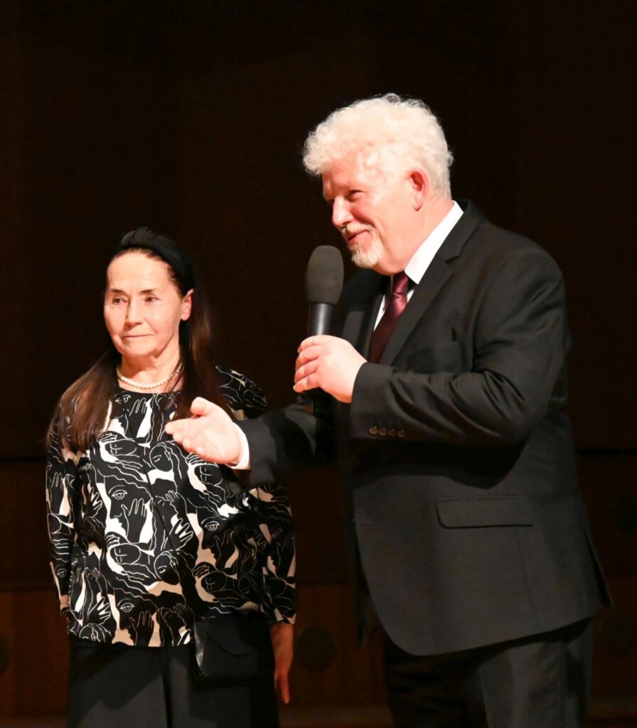 Mężczyzna z mikrofonem stoi obok kobiety na scenie i przemawia do publiczności podczas gali (kliknięcie powiększy zdjęcie).