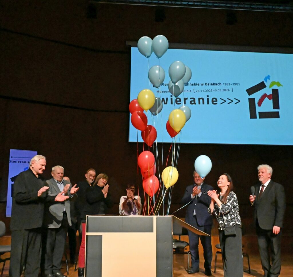 Uczestnicy wydarzenia na scenie wypuszczają kolorowe balony na tle ekranu z tytułem wydarzenia (kliknięcie powiększy zdjęcie).
