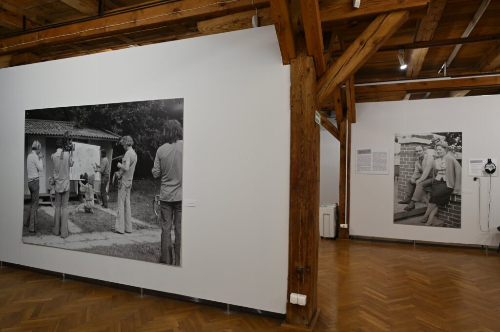 Fragment wystawy z dużymi czarno-białymi fotografiami dokumentalnymi; na zdjęciach przedstawiono grupy osób podczas spotkań i wydarzeń w plenerze, a obok fotografii umieszczono materiały tekstowe i niewielkie reprodukcje (kliknięcie powiększy zdjęcie).