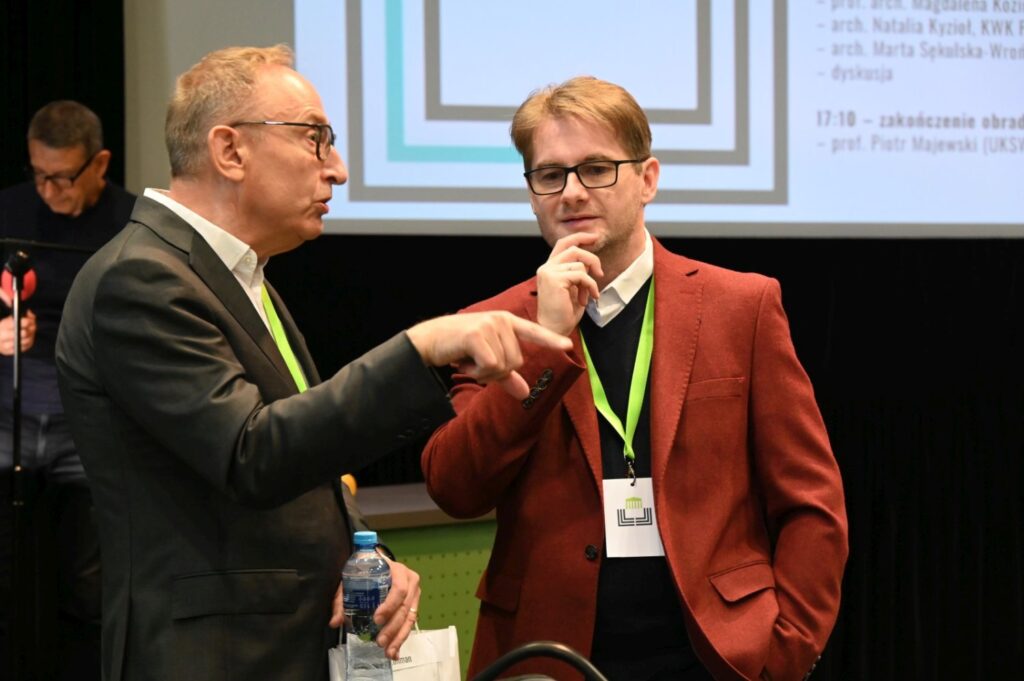 Dwóch uczestników konferencji rozmawia podczas przerwy, jeden z nich wskazuje coś ręką (kliknięcie powiększy zdjęcie).