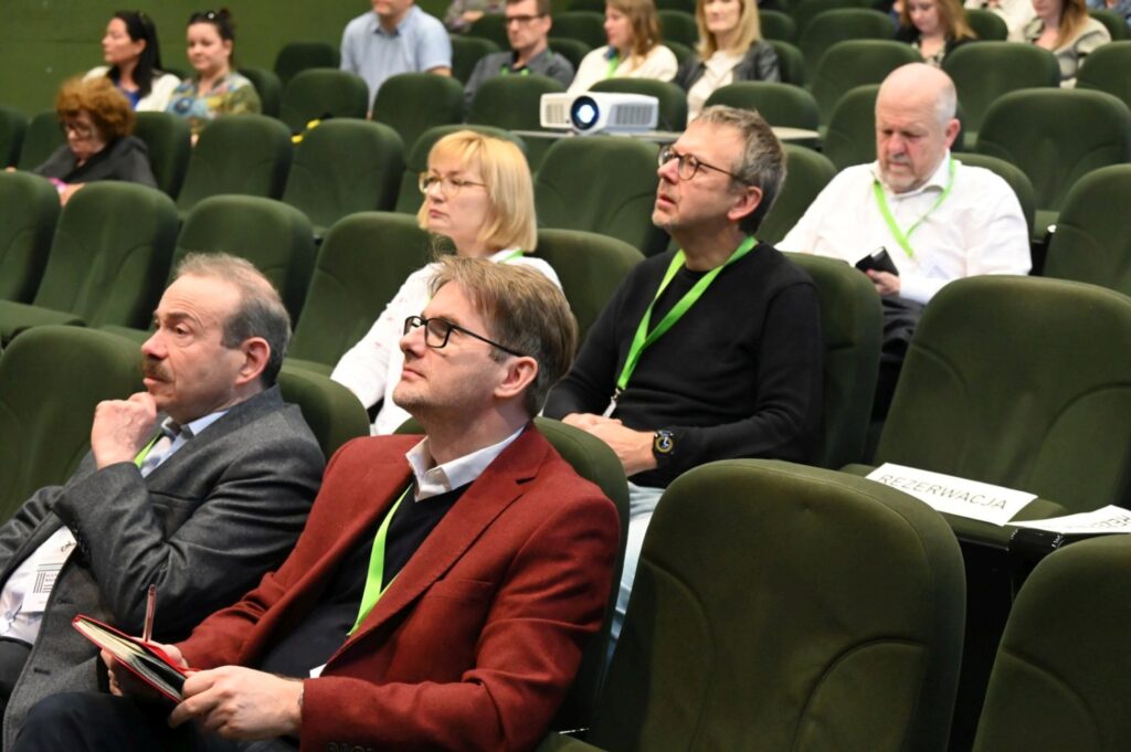 Uczestnicy konferencji siedzą w fotelach i uważnie słuchają prezentacji, patrząc w stronę sceny (kliknięcie powiększy zdjęcie).