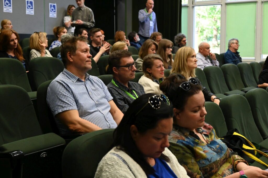 Publiczność wypełnia salę konferencyjną, skupiona na prelekcji odbywającej się na scenie (kliknięcie powiększy zdjęcie).