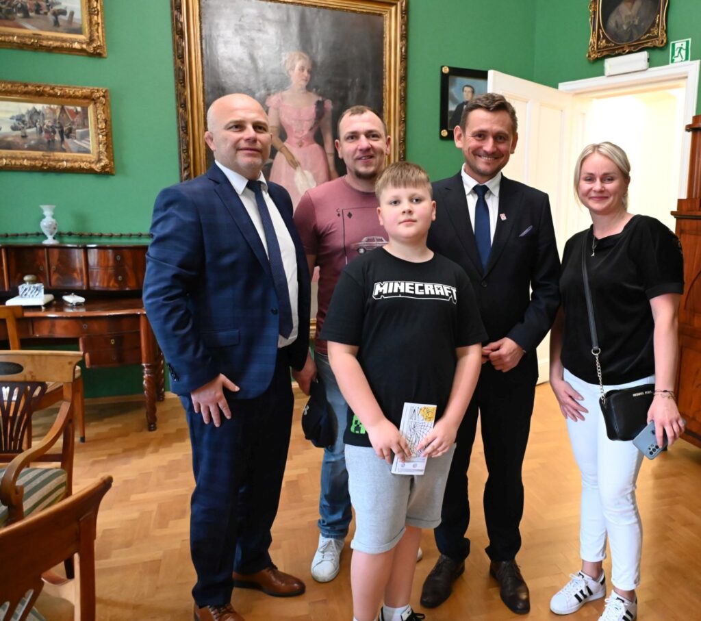 Grupa osób pozuje do zdjęcia w sali muzealnej z obrazami i zabytkowym wyposażeniem (kliknięcie powiększy zdjęcie).