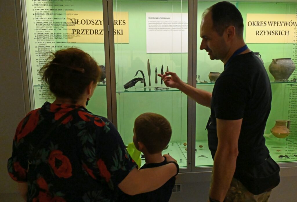 Mężczyzna pokazuje dziecku eksponaty w przeszklonej gablocie, tłumacząc ich znaczenie podczas zwiedzania (kliknięcie powiększy zdjęcie).