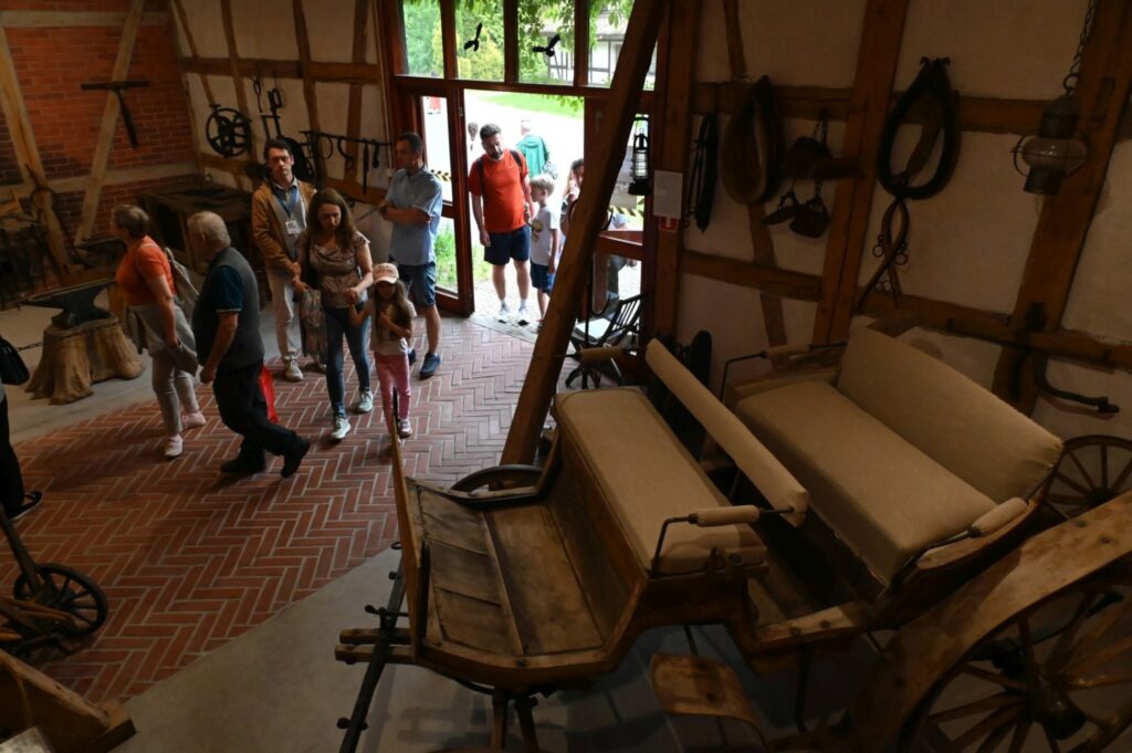 Zwiedzający przechodzą przez wystawę "Kuźnia pomorska" z eksponatami technicznymi i drewnianą konstrukcją (kliknięcie powiększy zdjęcie).