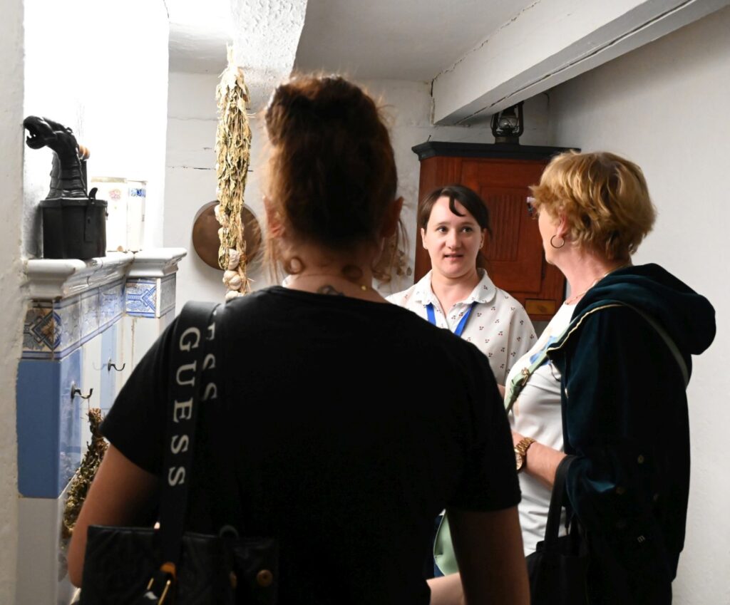 Przewodniczka rozmawia z dwiema kobietami w zabytkowej kuchni, objaśniając elementy dawnego wyposażenia (kliknięcie powiększy zdjęcie).