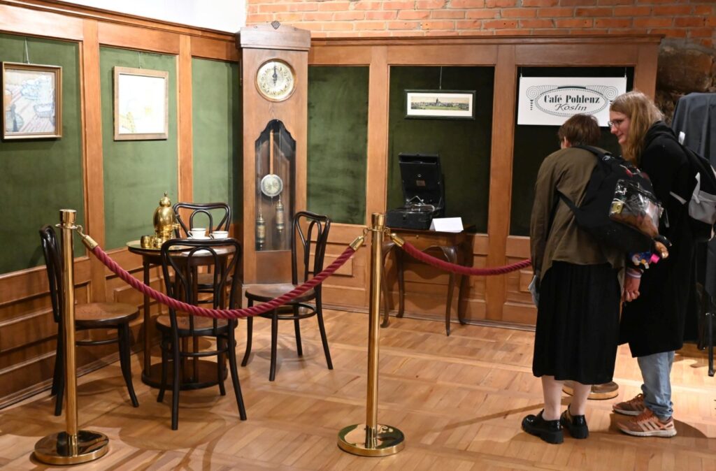 Zwiedzający oglądają zaaranżowane wnętrze historyczne oddzielone barierką, z meblami i zegarem (kliknięcie powiększy zdjęcie).