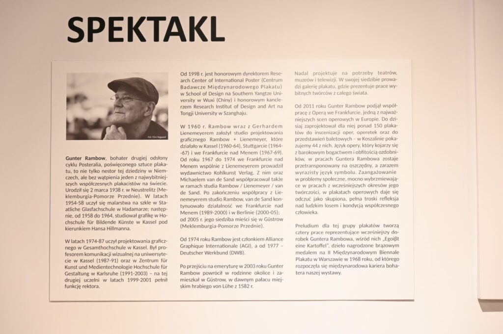 Plansza informacyjna zatytułowana „Spektakl”; na planszy znajduje się biograficzny i kuratorski tekst poświęcony Gunterowi Rambowowi oraz jego twórczości plakatowej; obok informacji tekstowych umieszczono fotografię artysty (kliknięcie powiększy zdjęcie).