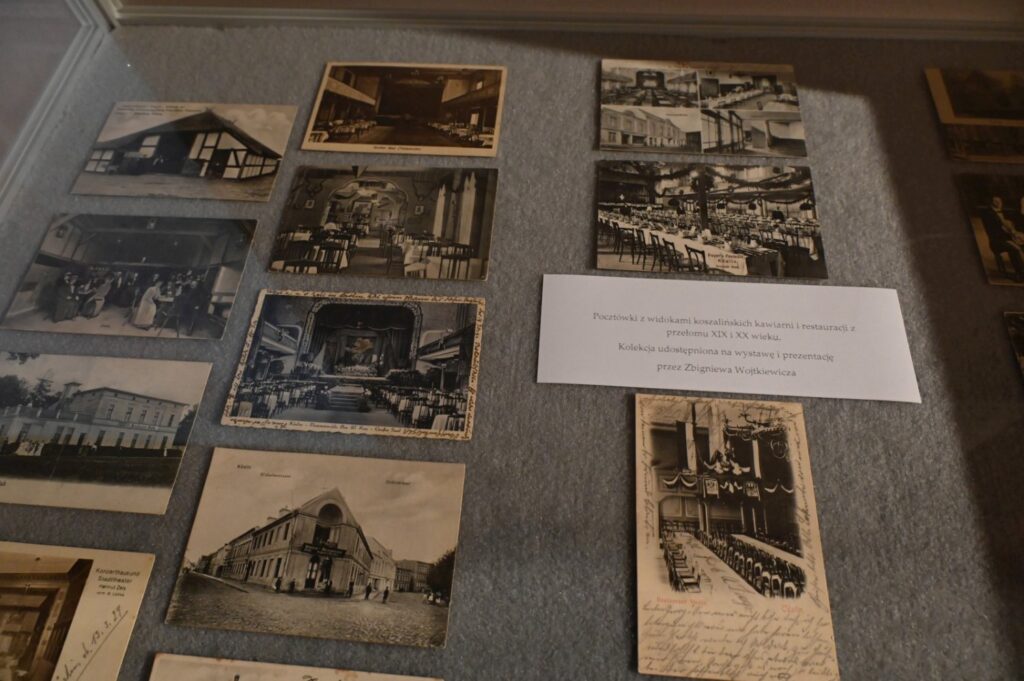 Fragment ekspozycji z archiwalnymi fotografiami budynków i wnętrz oraz pocztówkami; pośrodku umieszczono tabliczkę z opisem dotyczącym historii lokalnych zakładów i obiektów (kliknięcie powiększy zdjęcie).