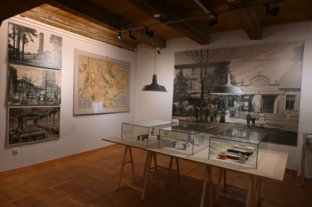 Fragment ekspozycji poświęconej historii miasta; na ścianach wiszą archiwalne fotografie i mapa, a w przeszklonych gablotach na środku sali prezentowane są zabytkowe przedmioty (kliknięcie powiększy zdjęcie).