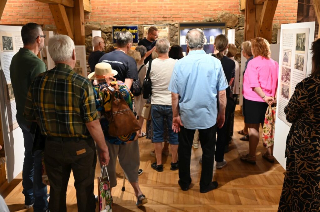 Zwiedzający oglądają ekspozycję podczas finisażu; liczna grupa osób zgromadziła się przy planszach i gablotach z historycznymi eksponatami (kliknięcie powiększy zdjęcie).