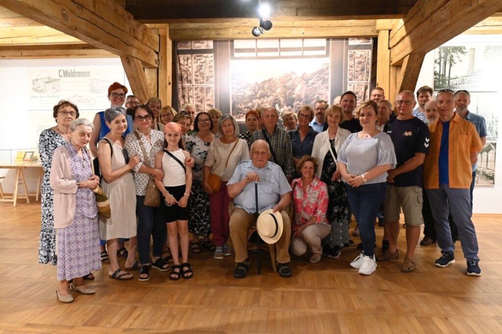 Wspólne zdjęcie uczestników finisażu; liczna grupa osób stoi i siedzi przed ekspozycją w sali wystawowej, w tle widoczne są plansze oraz duża fotografia historyczna (kliknięcie powiększy zdjęcie).