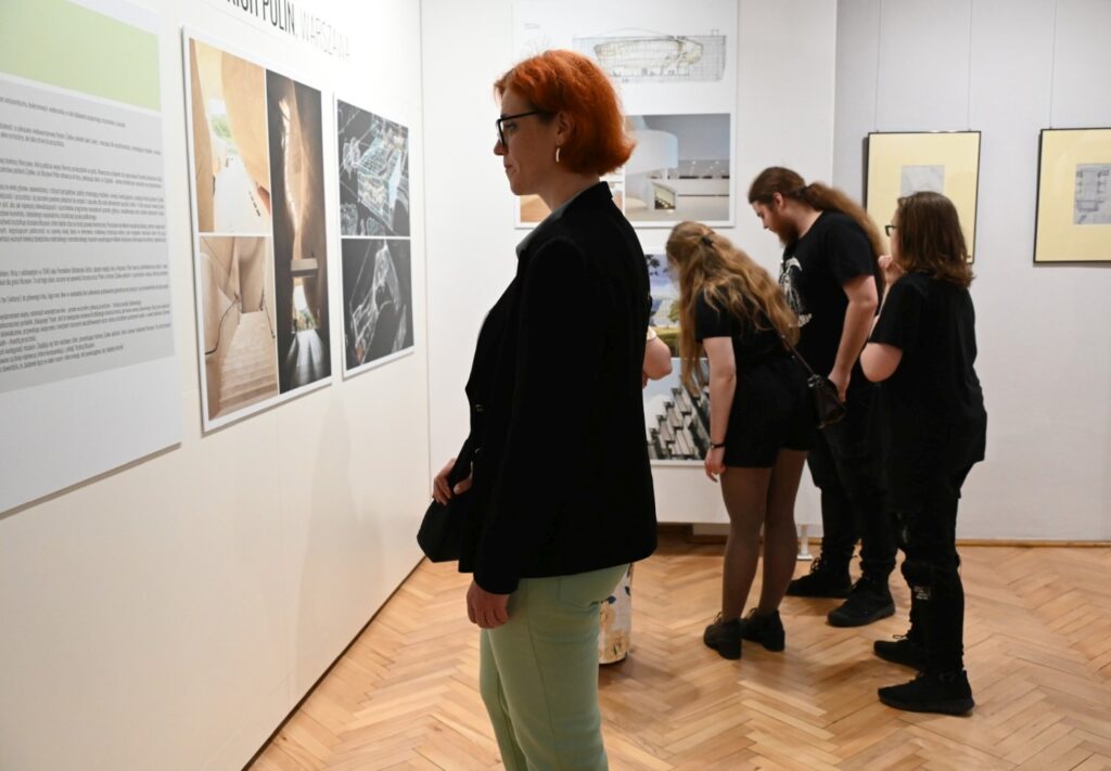 Zwiedzający oglądają plansze z projektami architektonicznymi zawieszone na ścianie galerii (kliknięcie powiększy zdjęcie).