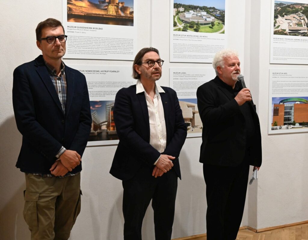 Trzech mężczyzn stoi przed planszami wystawowymi, jeden z nich przemawia do zgromadzonych gości (kliknięcie powiększy zdjęcie).