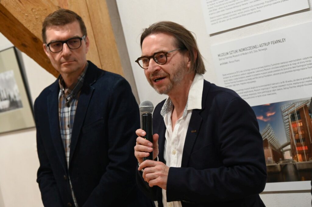 Mężczyzna trzyma mikrofon i przemawia podczas wernisażu, obok stoi drugi uczestnik wydarzenia (kliknięcie powiększy zdjęcie).