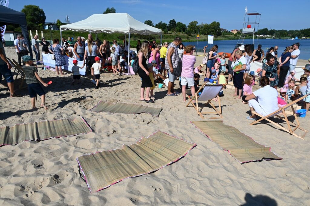 Grupa ludzi odpoczywa na leżakach i spaceruje po plaży podczas wydarzenia plenerowego (kliknięcie powiększy zdjęcie).