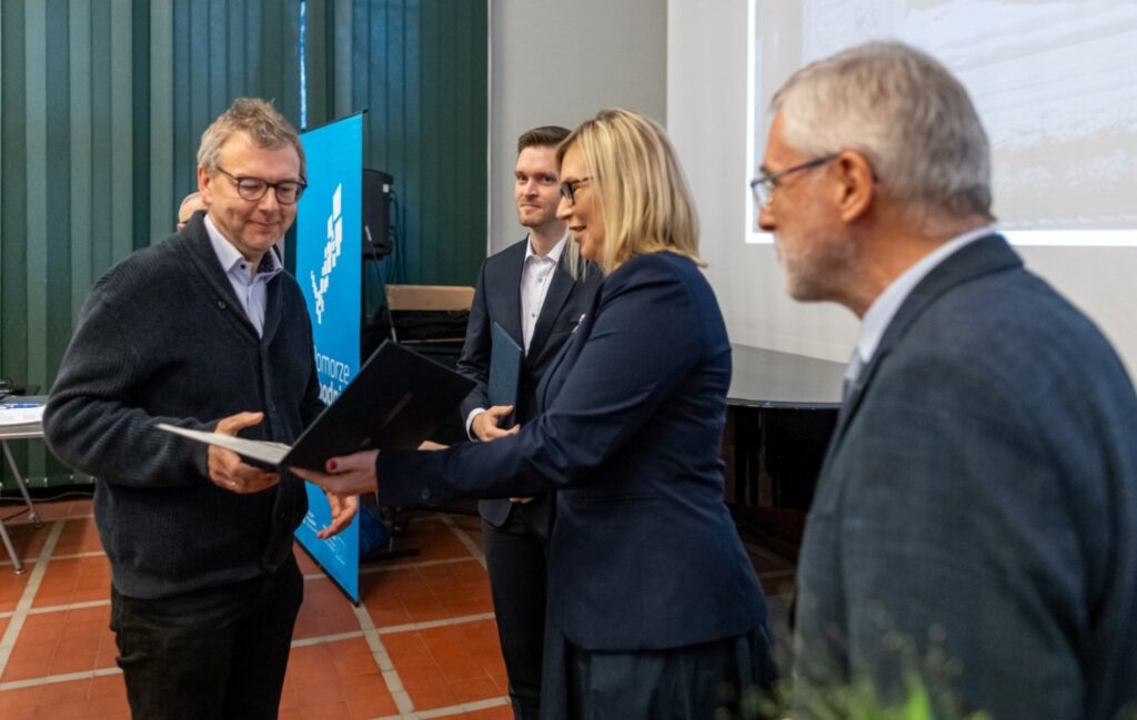 Kobieta wręcza nagrodę mężczyźnie, przekazując dyplom podczas uroczystości (kliknięcie powiększy zdjęcie).