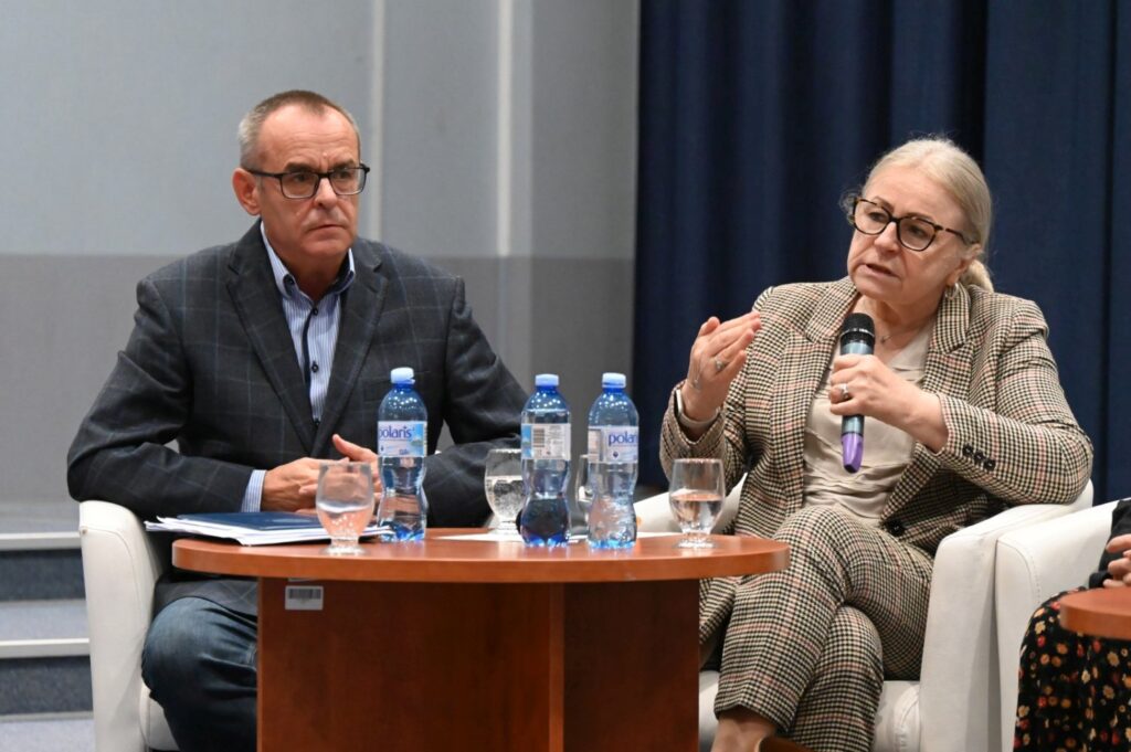 Dwoje panelistów siedzi przy stole i dyskutuje podczas panelu konferencyjnego (kliknięcie powiększy zdjęcie).