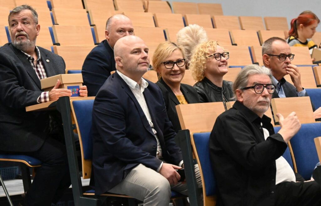 Grupa uczestników konferencji siedzi w rzędach, część z nich patrzy w stronę sceny (kliknięcie powiększy zdjęcie).