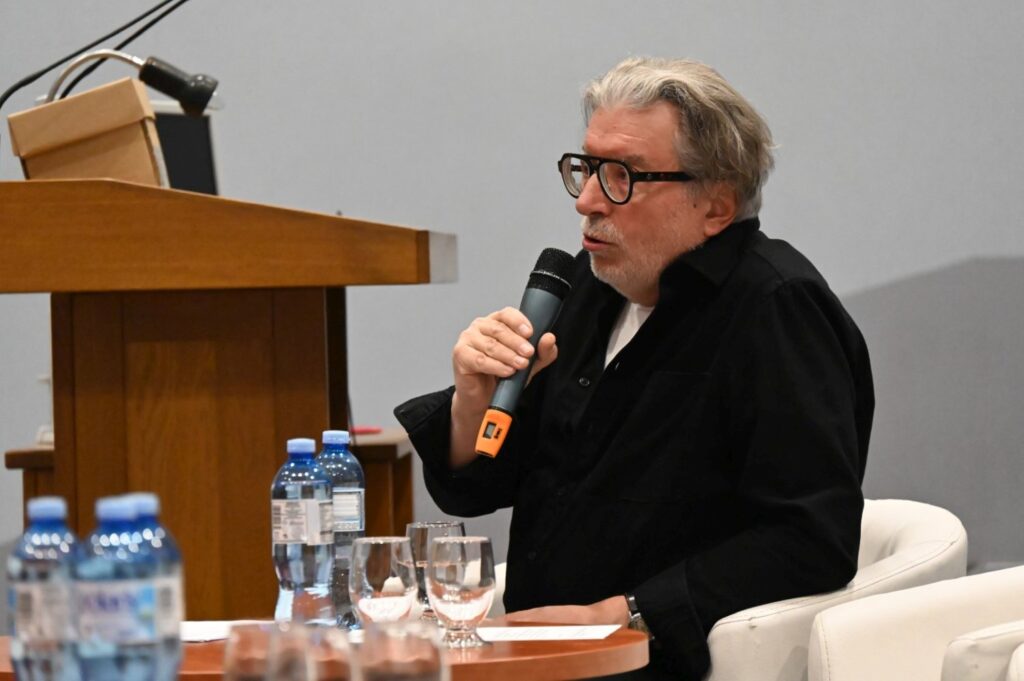 Mężczyzna siedzi przy stole i mówi do mikrofonu podczas panelu dyskusyjnego (kliknięcie powiększy zdjęcie).