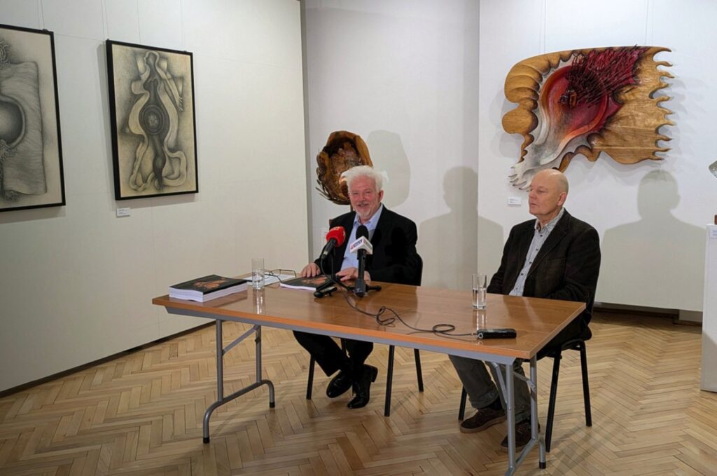 Dwóch mężczyzn siedzi przy stole i udziela wypowiedzi podczas konferencji prasowej na tle eksponowanych dzieł sztuki (kliknięcie powiększy zdjęcie).