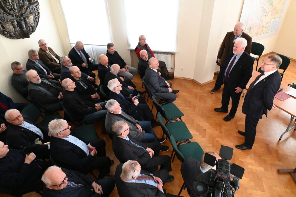 Uroczyste otwarcie wystawy z udziałem zaproszonych gości; w sali zgromadzona jest liczna publiczność, a w centralnej części spotkania kilka osób stoi przed siedzącymi uczestnikami; wydarzenie jest dokumentowane przez fotografów i operatorów kamer (kliknięcie powiększy zdjęcie).