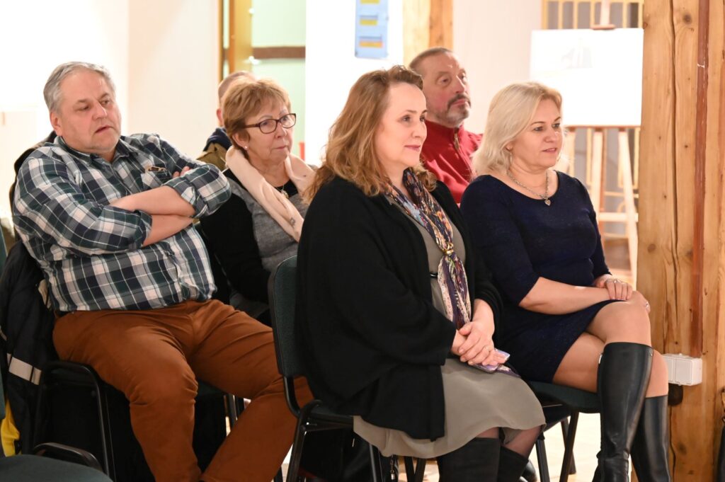 Uczestnicy konferencji siedzący w pierwszym rzędzie uważnie słuchają wystąpienia w sali wystawowej (kliknięcie powiększy zdjęcie).