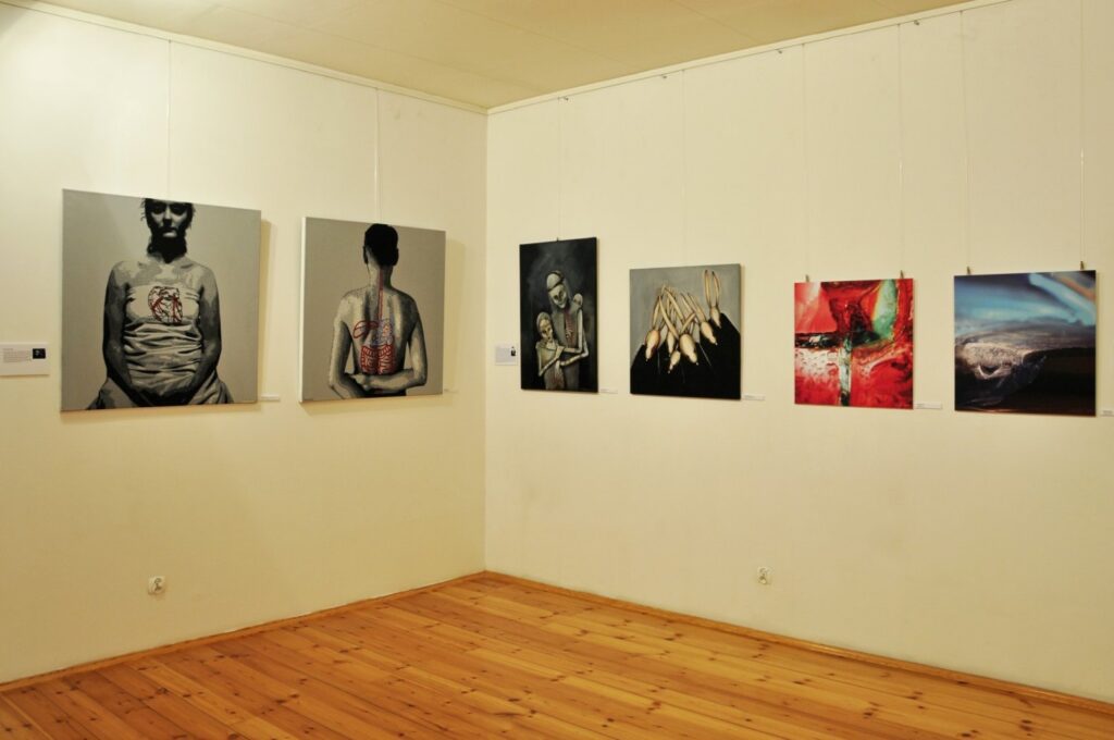Fragment wystawy prezentujący obrazy i prace współczesnych artystów eksponowane na ścianie galerii (kliknięcie powiększy zdjęcie).