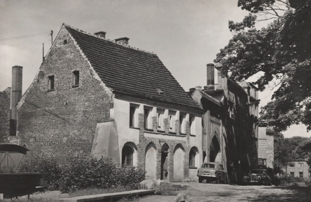 Czarno-biała fotografia Domku Kata na pocztówce wydanej w 1966 roku; przed budynkiem z charakterystycznym ceglanym szczytem stoją samochody, a w tle widoczna jest dalsza zabudowa (kliknięcie powiększy zdjęcie).