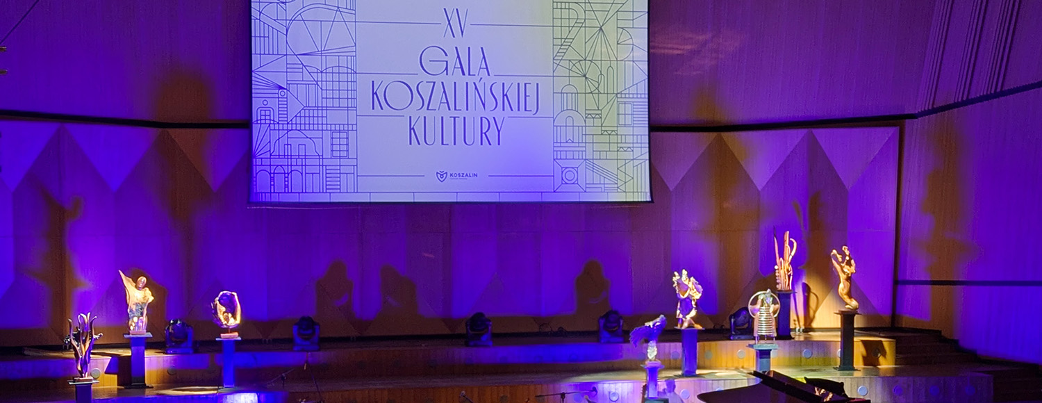 Scena XV Gali Koszalińskiej Kultury; na podestach rozmieszczono statuetki i rzeźby, a nad sceną wyświetlany jest ekran z nazwą wydarzenia i jego jubileuszową edycją, całość utrzymana jest w fioletowej oprawie świetlnej (kliknięcie powiększy zdjęcie).