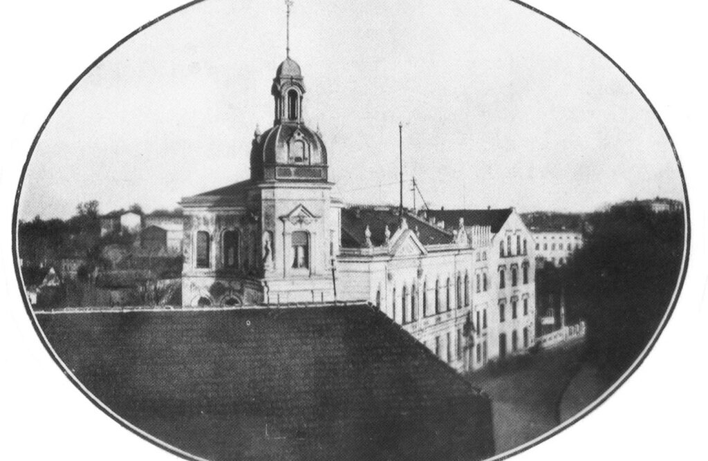 Archiwalna fotografia budynku obecnego Muzeum w Koszalinie z 1929 roku; czarno-białe zdjęcie przedstawia budynek z charakterystyczną wieżą i kopułą, widziany z sąsiedniej zabudowy (kliknięcie powiększy zdjęcie).